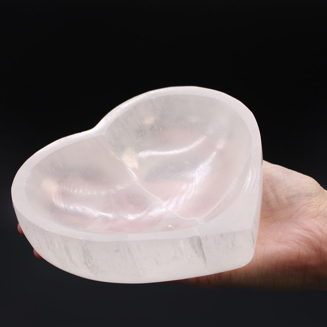 Heart-shaped crystal held in a hand against a black background