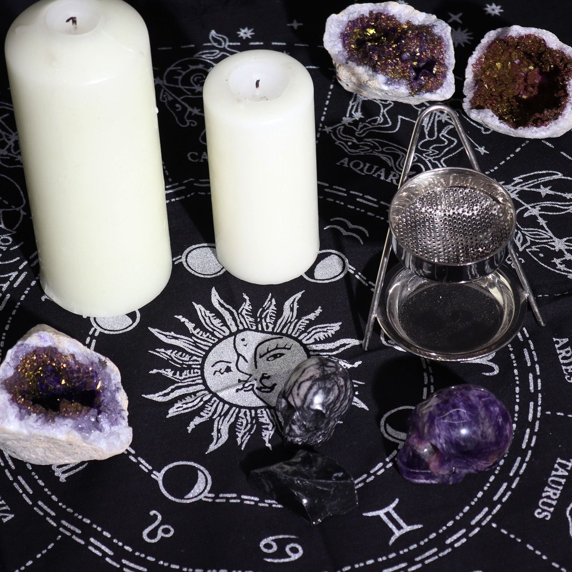 Decorative setting with candles, crystals, and a sun symbol on a black cloth with astrological symbols.