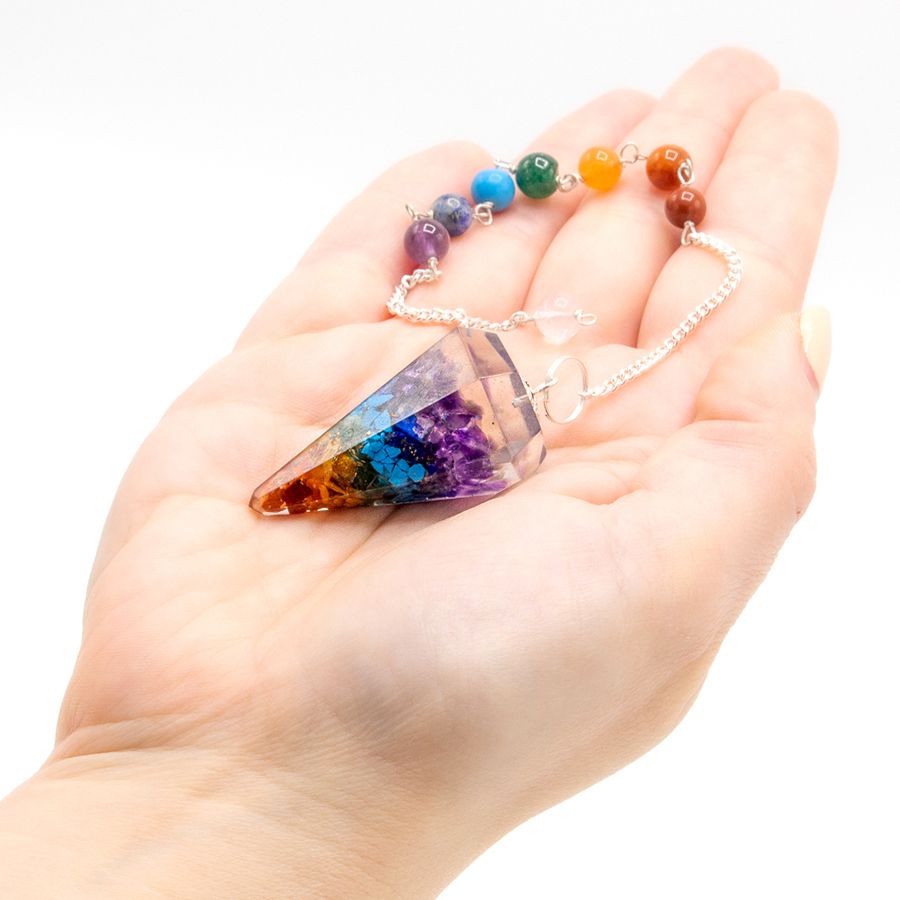 Colorful crystal pendant on a chain held in a hand against a white background