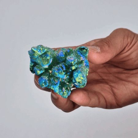 Hand holding a green and blue crystal against a plain background