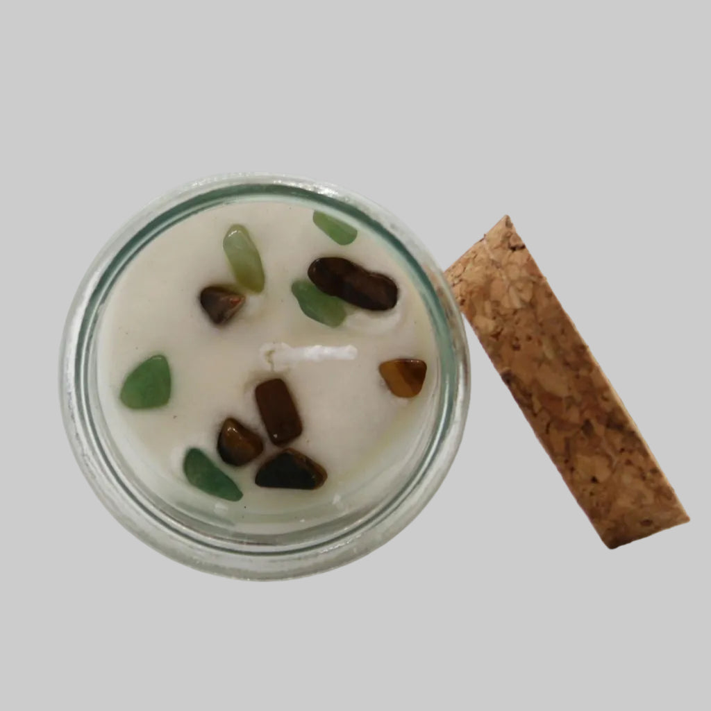 Candle in a glass jar with decorative stones and a cork lid on a white background