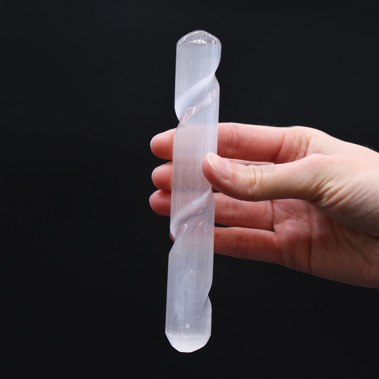 Hand holding a clear crystal against a black background