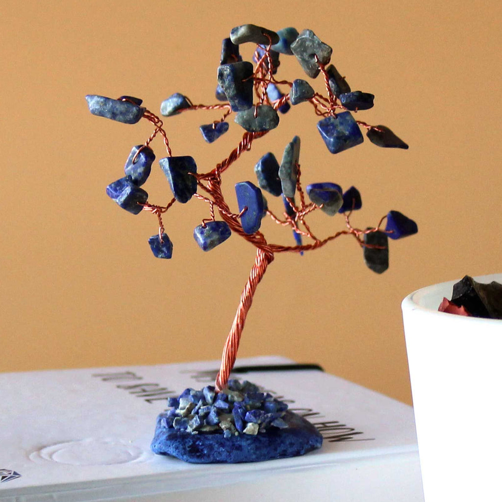 Decorative tree made of copper and blue stones on a book with a white container in the background.