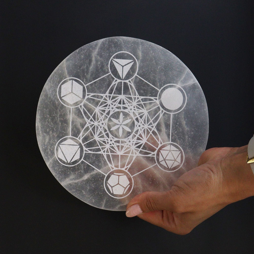 Hand holding a round stone with geometric design against a black background