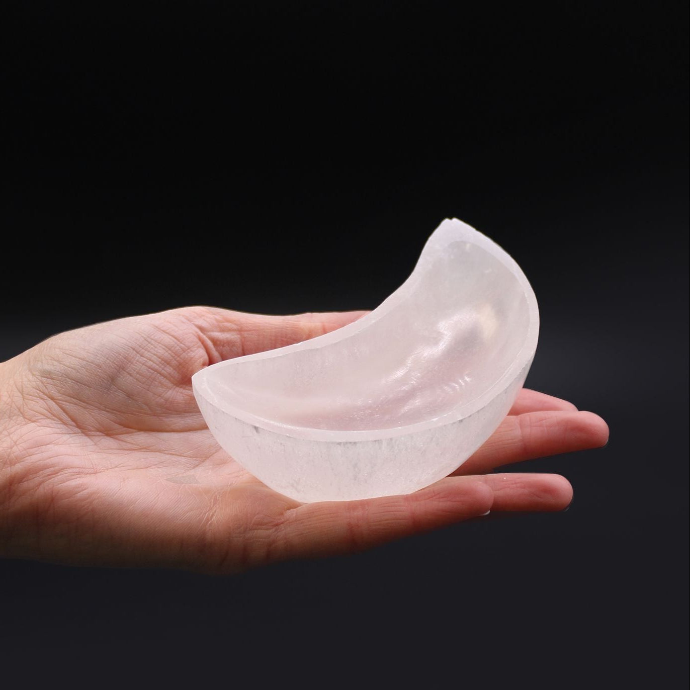 Clear silicone breast implant held in a hand against a black background