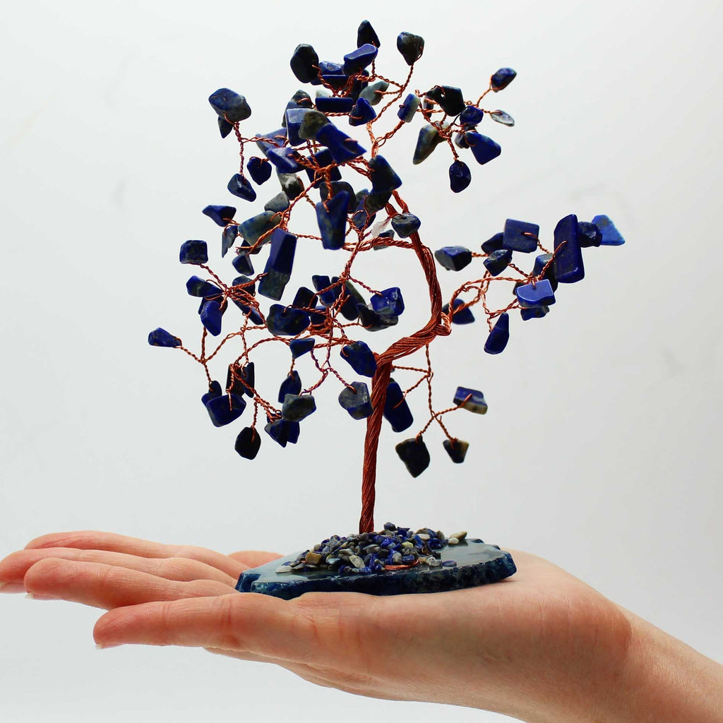 Hand holding a small tree sculpture with blue stones against a white background