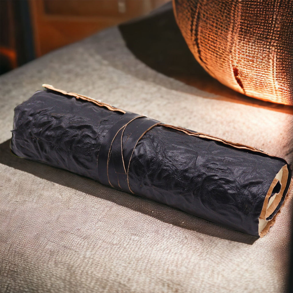 Rolled-up black paper or fabric with brown string on a textured surface