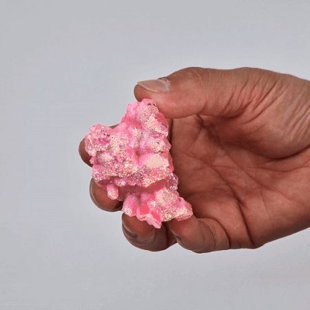 Hand holding a pink crystal against a plain background