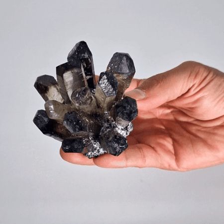 Hand holding a cluster of dark crystals against a light background