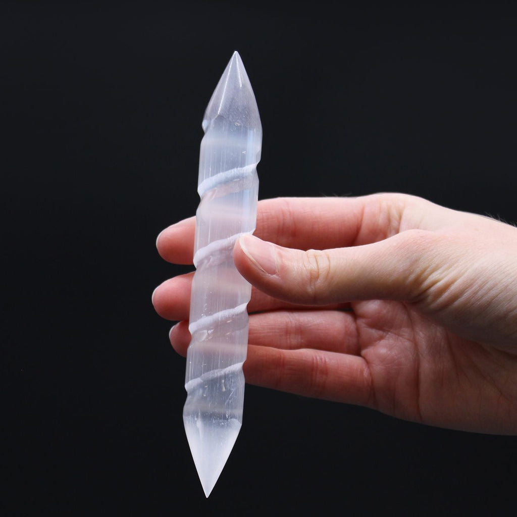 Hand holding a clear crystal pointed object against a black background