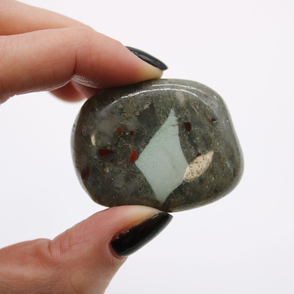 Hand holding a polished stone with a white center and red inclusions against a white background
