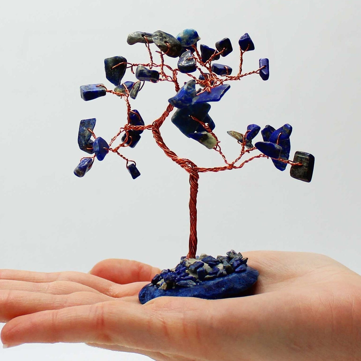 Hand holding a small tree sculpture with blue stones against a white background