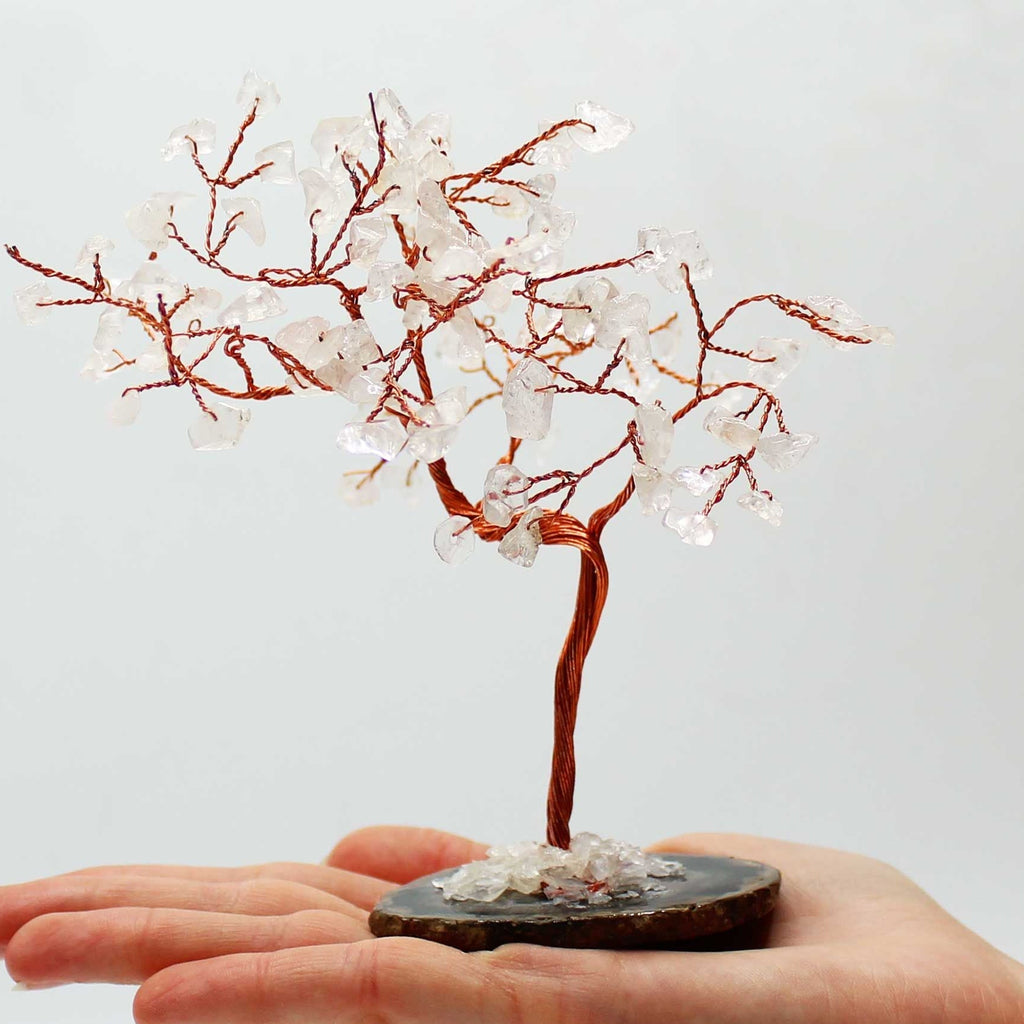 Small decorative tree with red branches and white beads on a hand against a light gray background
