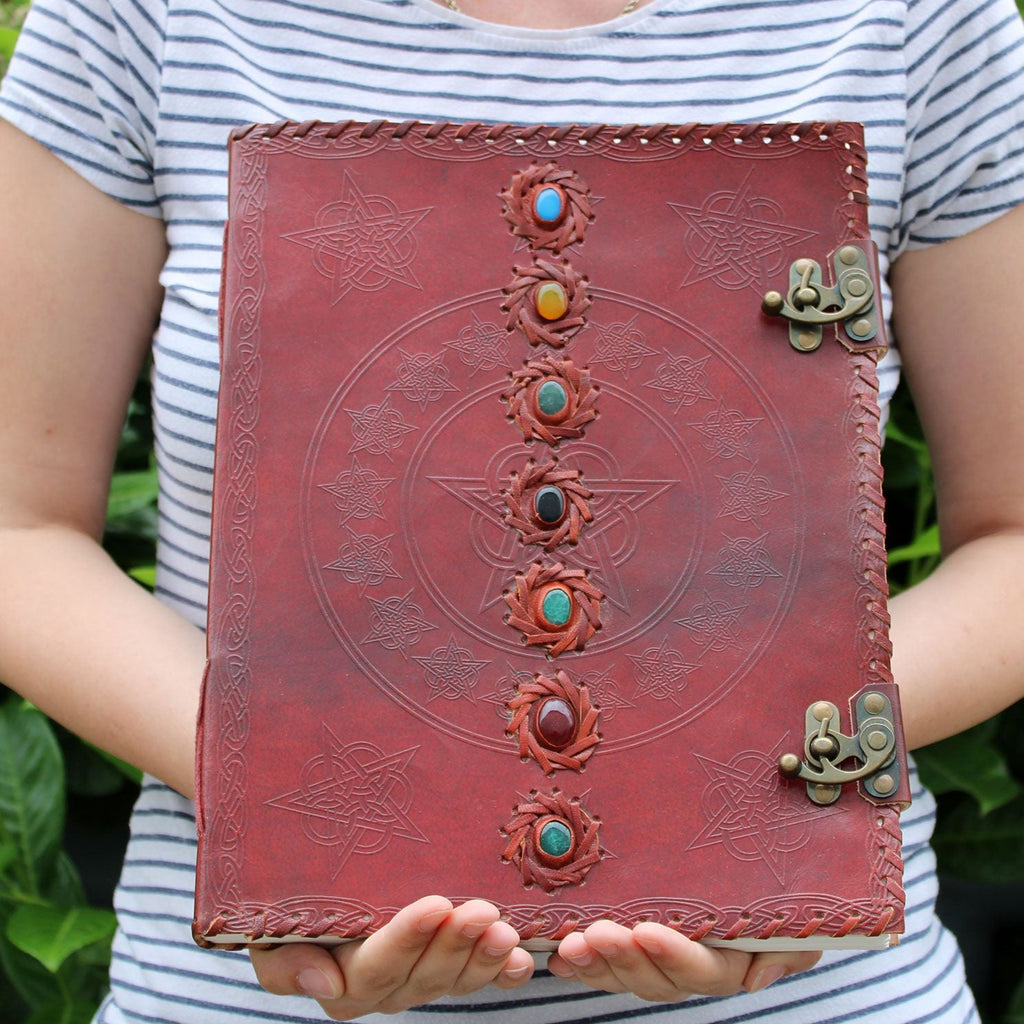 Person holding a red leather journal with embossed designs and colorful stones.