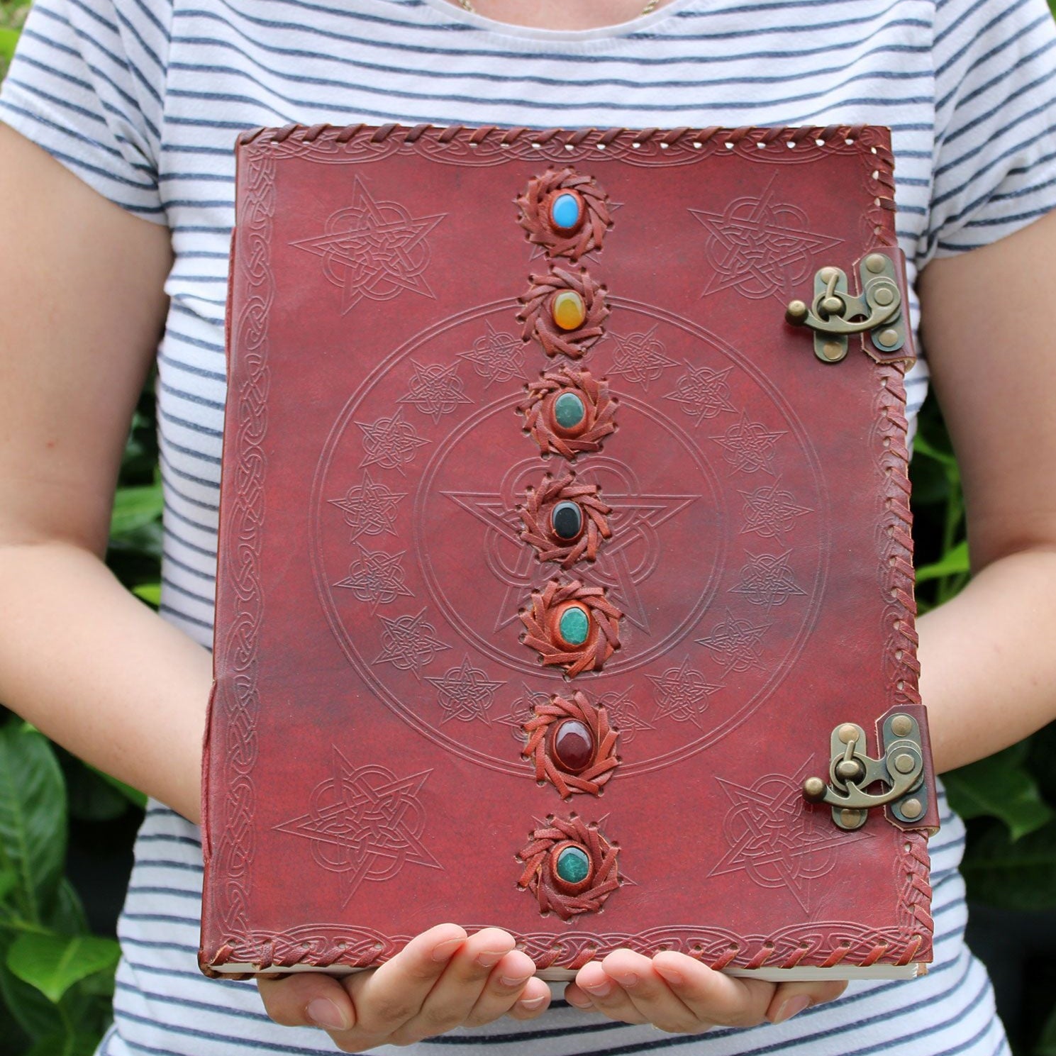 Person holding a red leather journal with embossed designs and colorful stones.