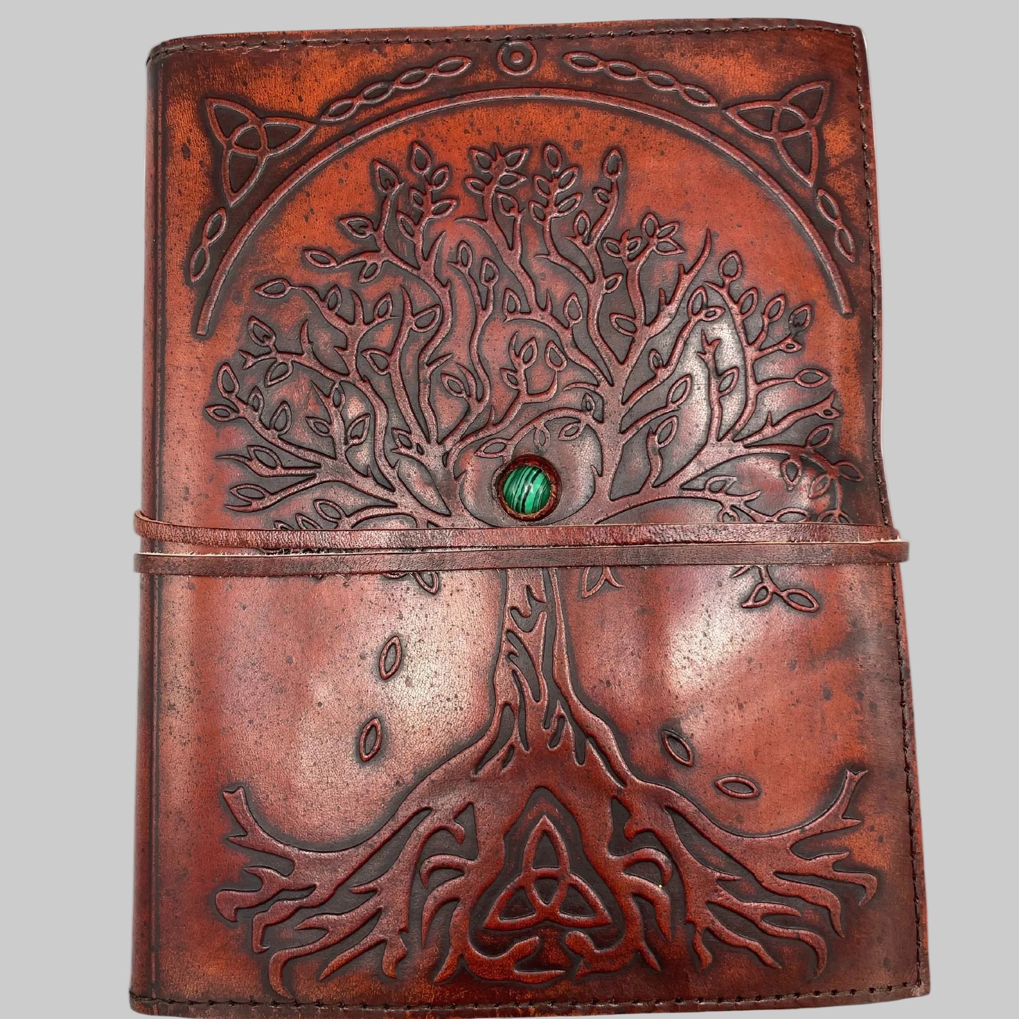 Brown leather journal with tree of life design and green gemstone on a white background