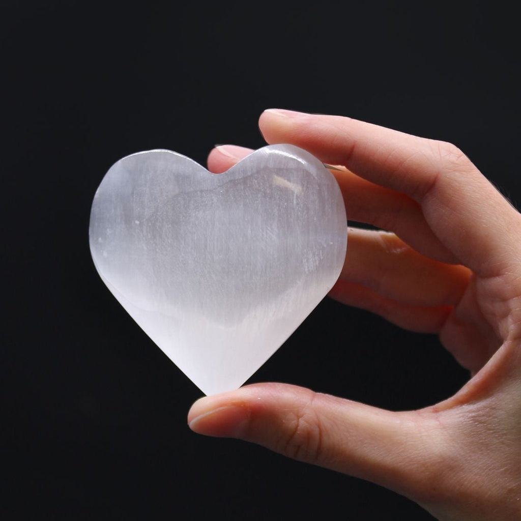 Hand holding a clear crystal heart against a black background