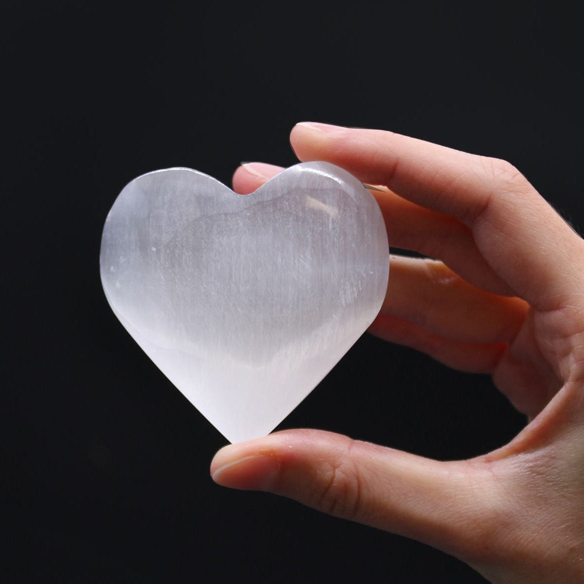 Hand holding a clear crystal heart against a black background