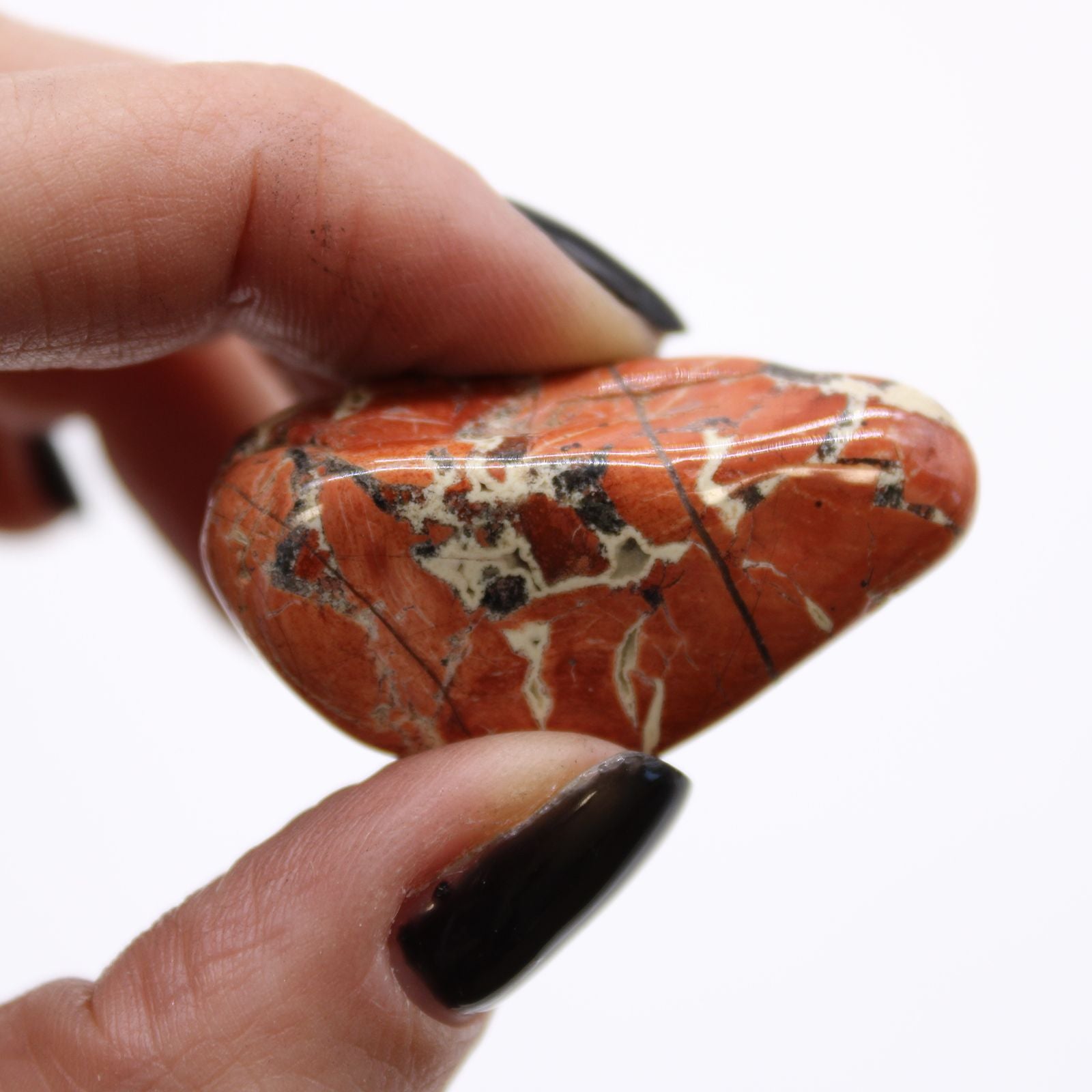 Hand holding a red jasper stone with white and black patterns on a white background