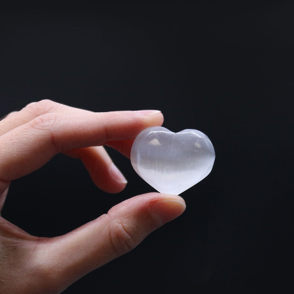 Hand holding a clear heart-shaped crystal against a black background