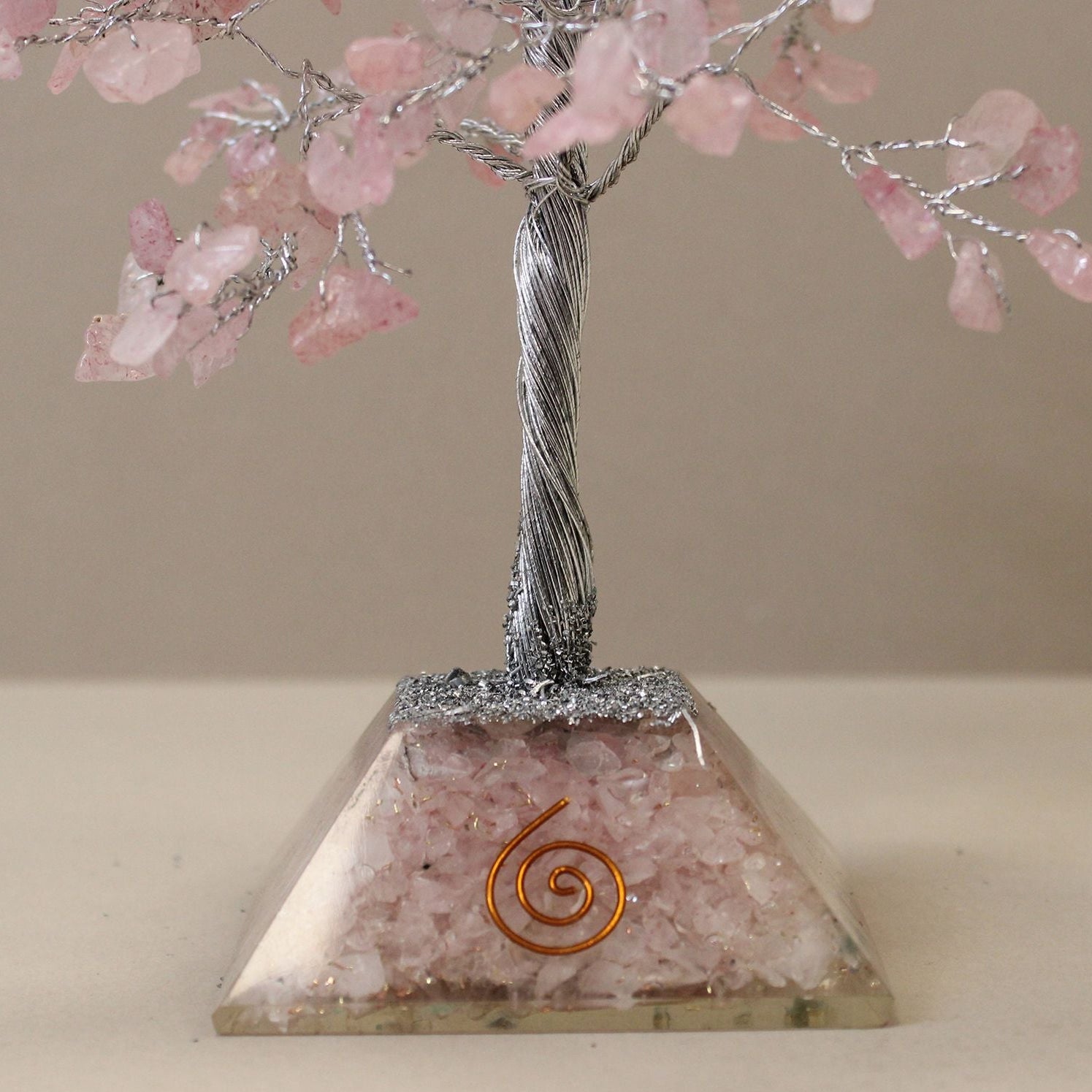 Decorative tree with pink blossoms on a pyramid-shaped base with a spiral design, against a plain background.