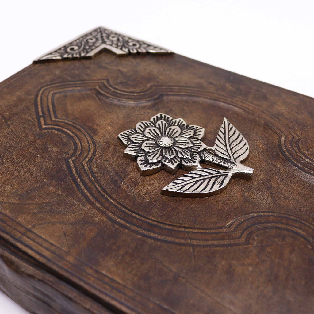 Brown leather-bound book with silver floral decoration on a white background