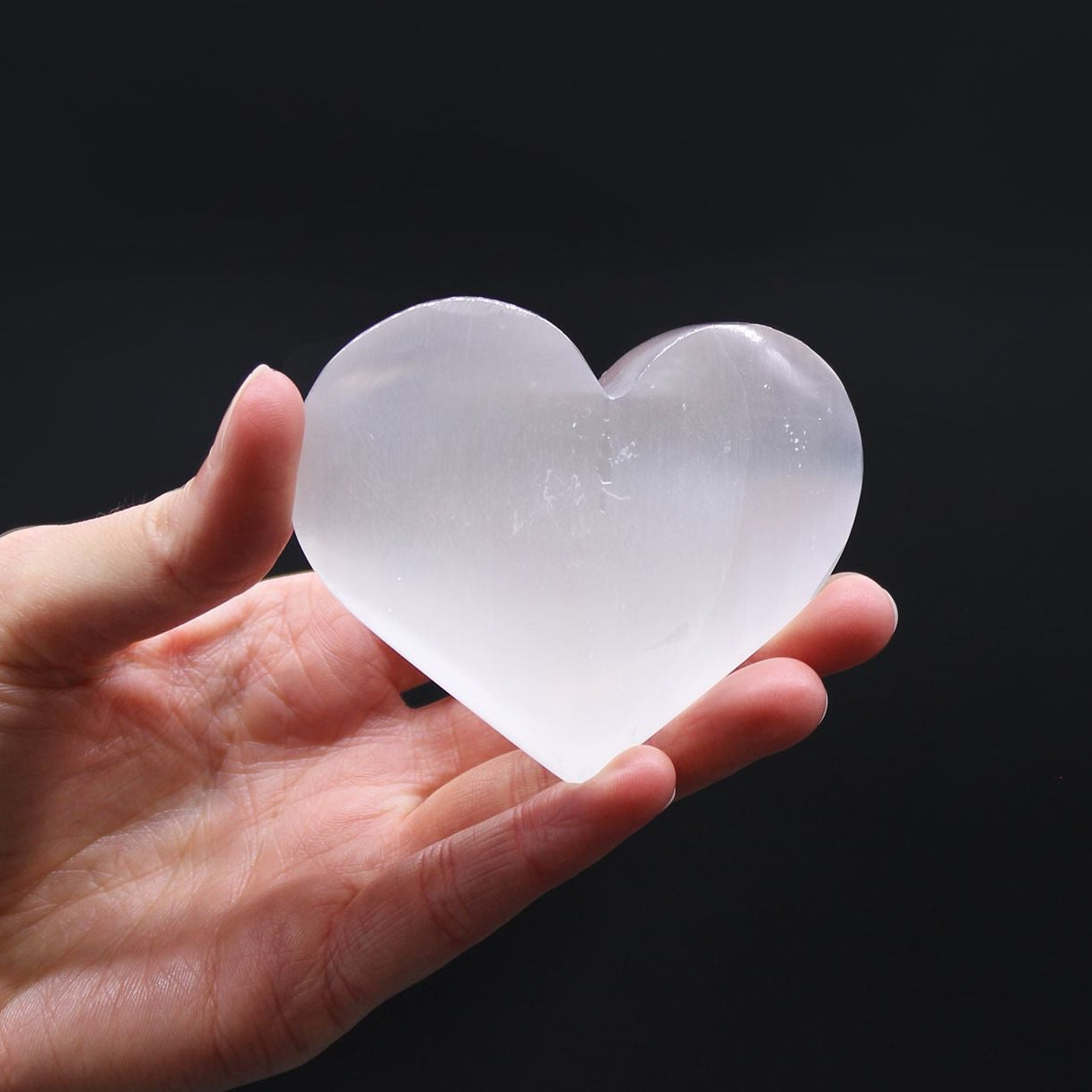 Hand holding a clear heart-shaped crystal against a black background
