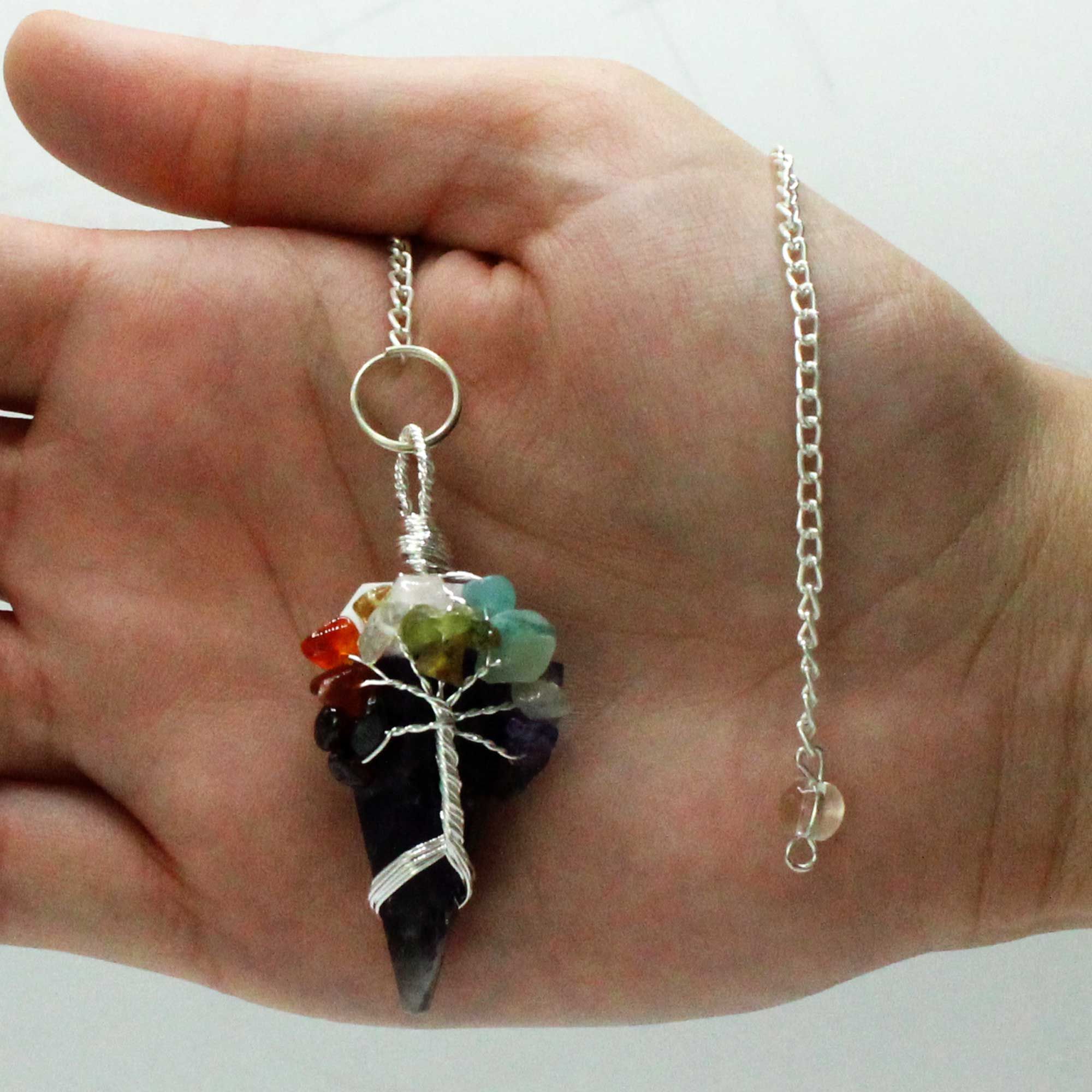 Hand holding a necklace with a multicolored stone pendant against a plain background