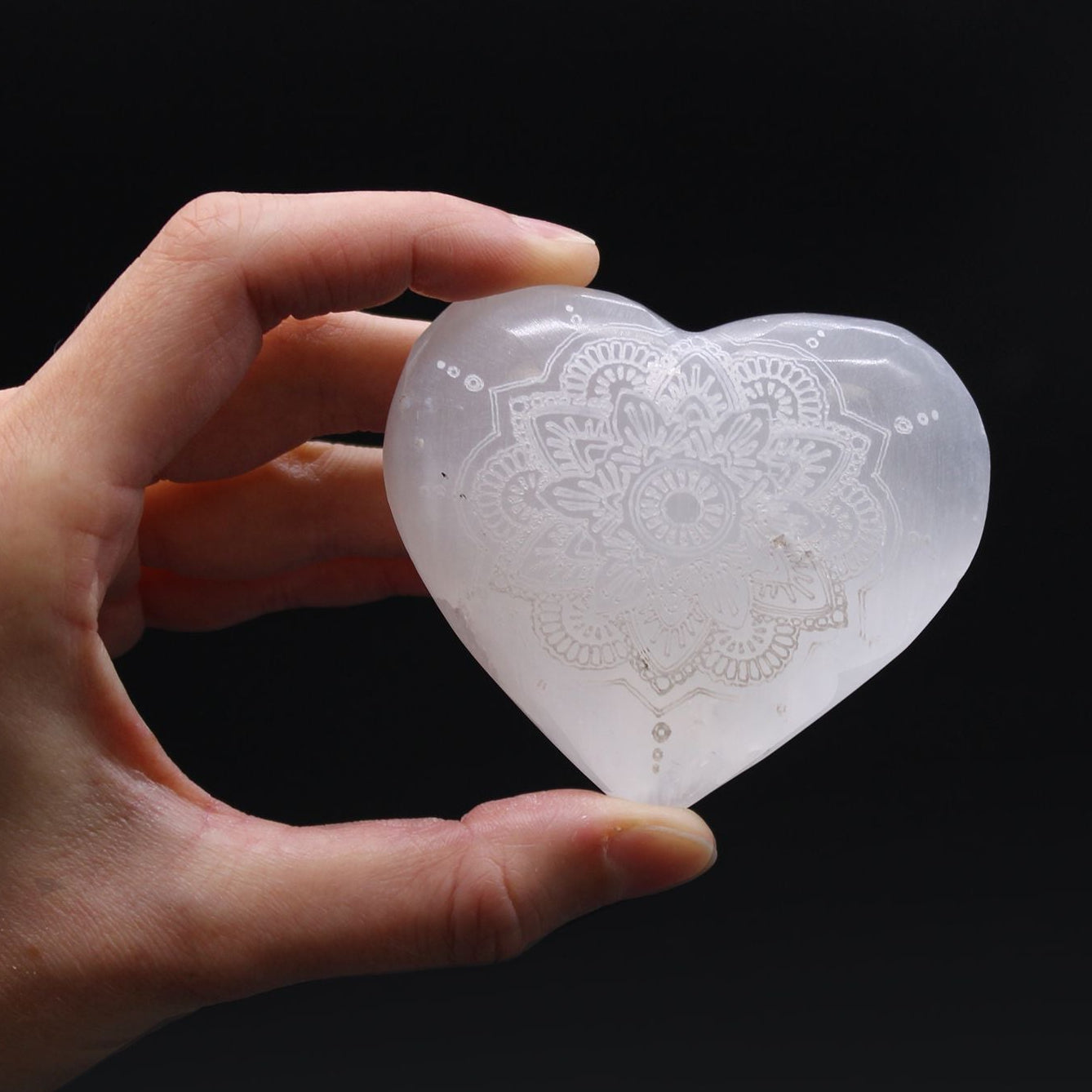 Heart-shaped crystal with mandala design held in a hand against a black background