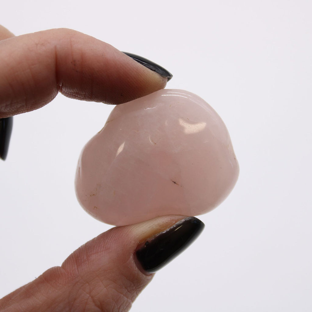 Hand holding a pink stone against a white background