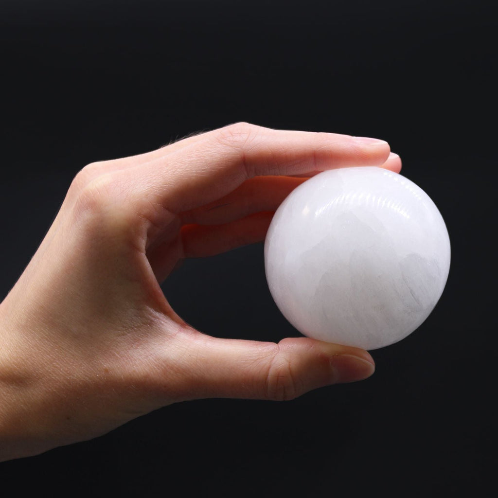 Hand holding a white spherical object against a black background