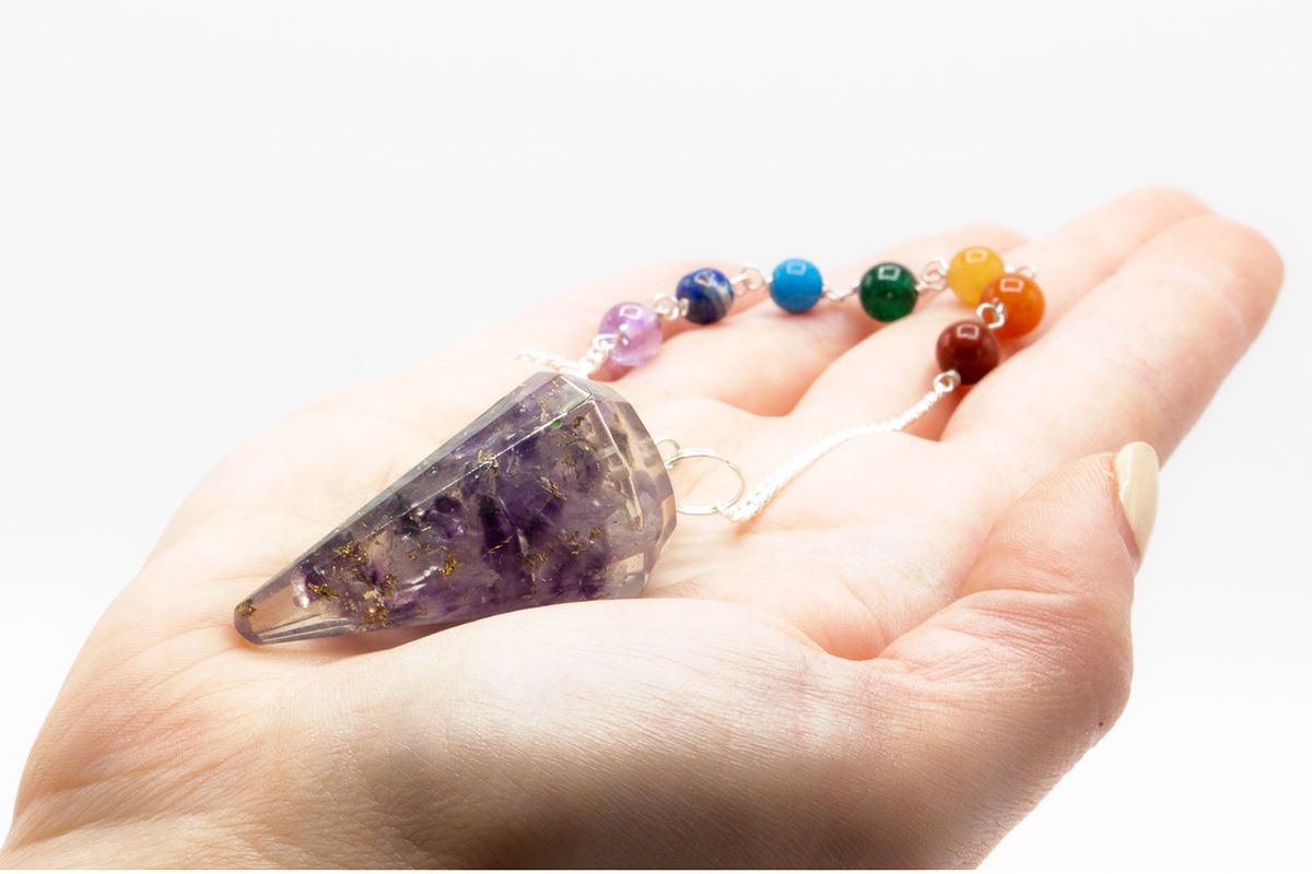 Hand holding a crystal pendulum with colorful beads on a white background