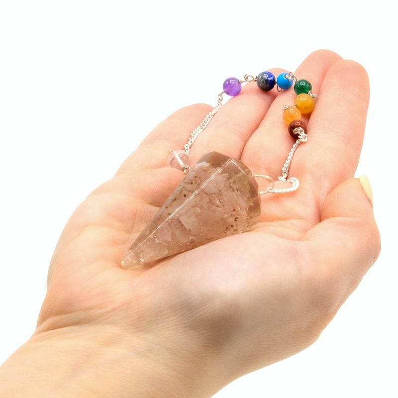 Crystal pendulum with colored beads held in a hand on a white background