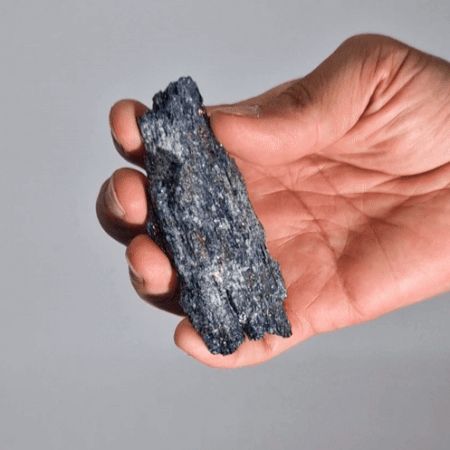 Hand holding a dark gray mineral against a plain background