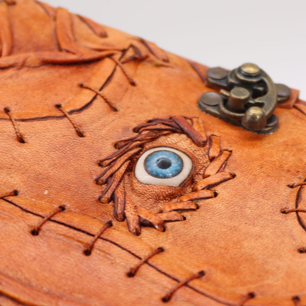 Brown leather pouch with eye design and metal clasp on a white background