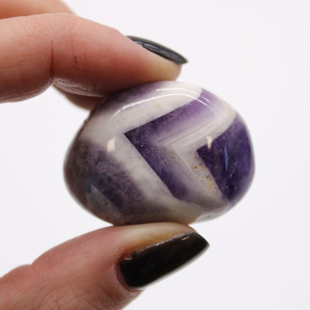 Hand holding a purple and white striped stone against a white background