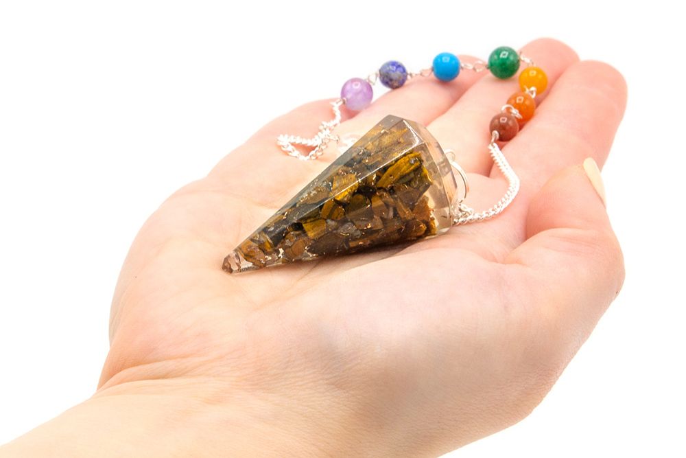 Hand holding a crystal pyramid with a colorful beaded necklace on a white background