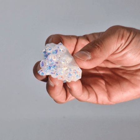 Hand holding a small, glittery crystal-like object against a plain background