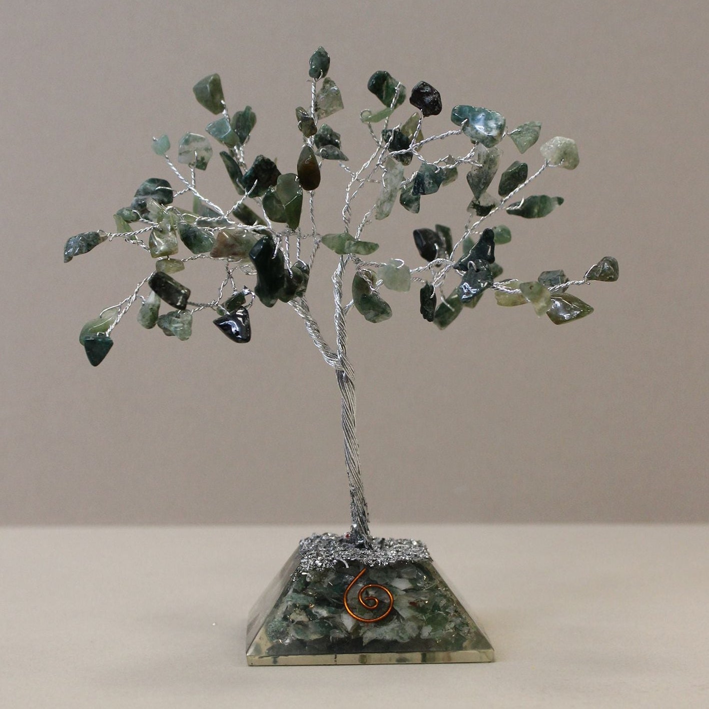 Decorative tree made of green stones on a beige base against a plain background