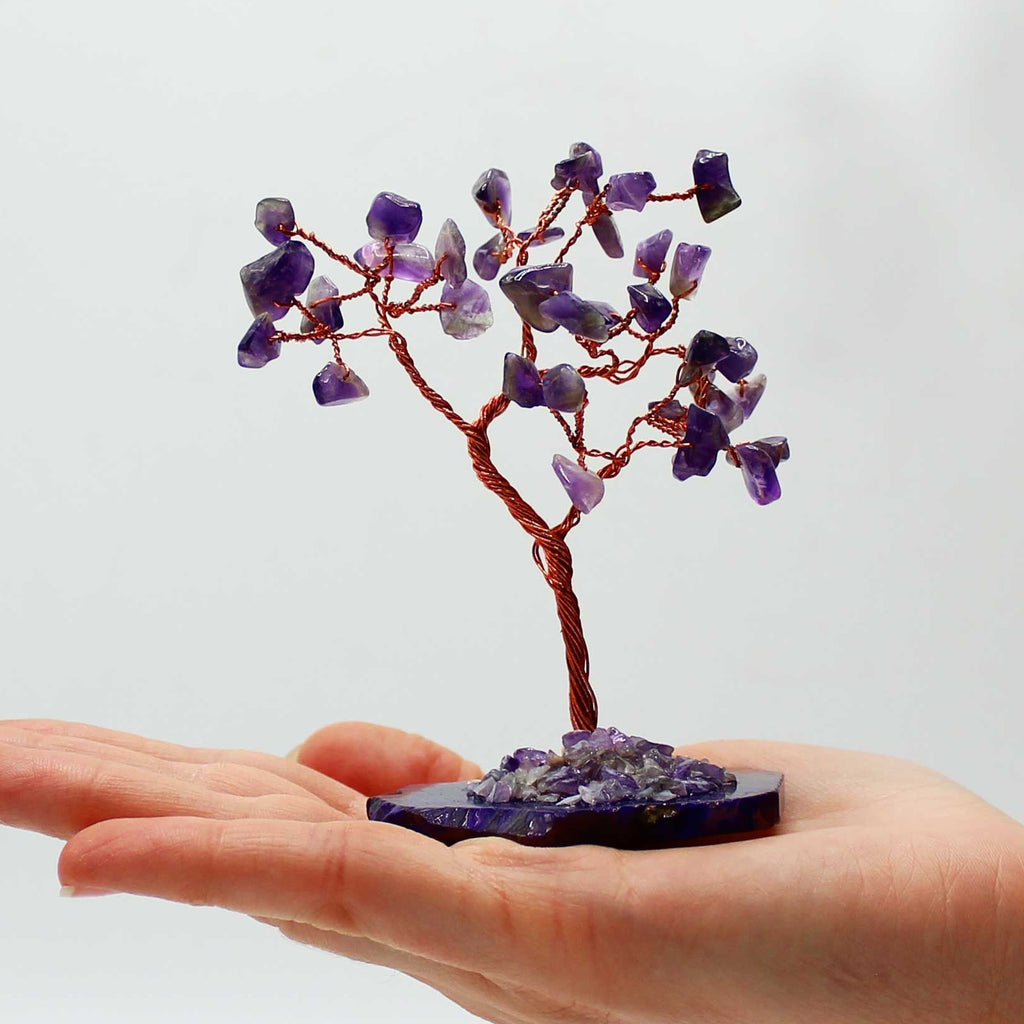 Hand holding a small tree sculpture made of purple stones on a white background