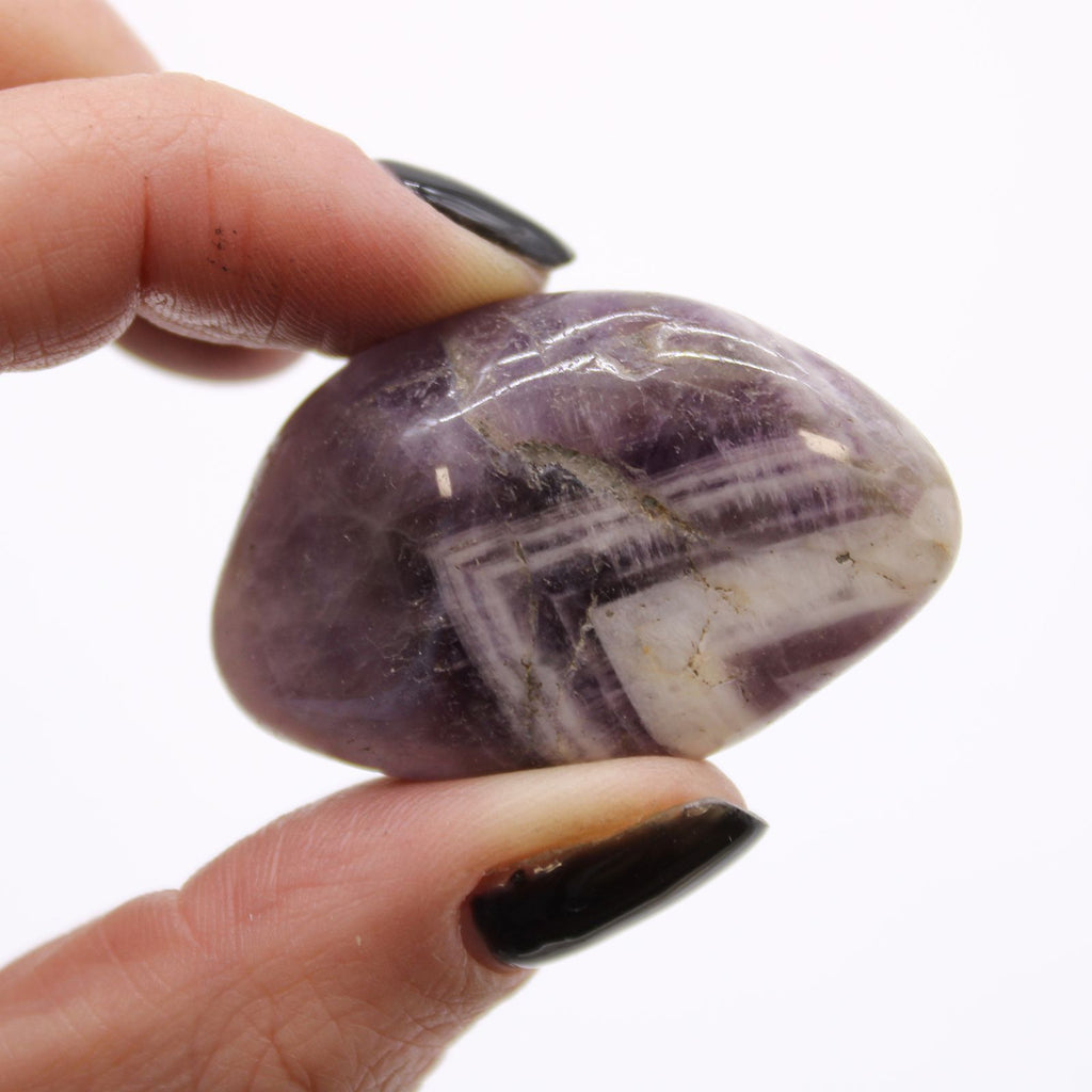 Hand holding a purple and white striped stone against a white background