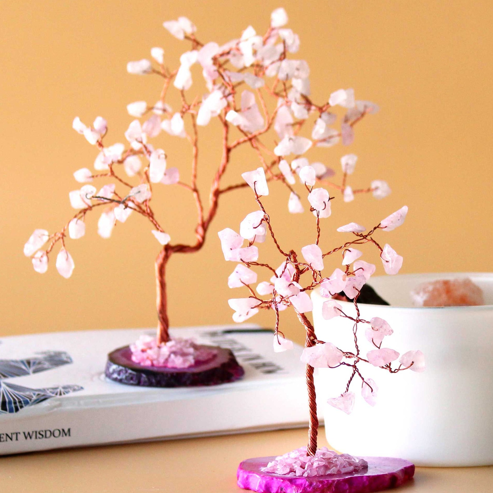 Decorative pink tree on a purple base with a book and white container in the background.