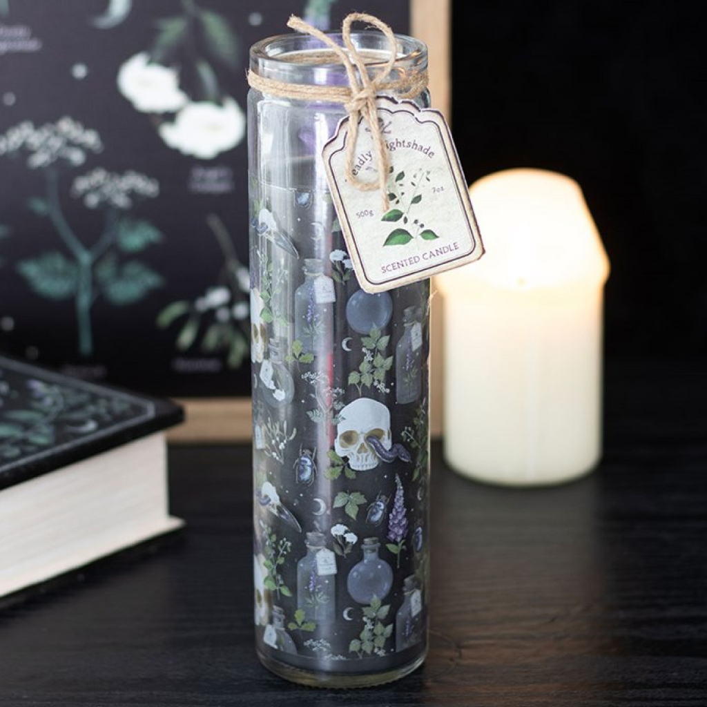 Decorative candle in a glass jar with a label on a dark surface, surrounded by books and a candle.