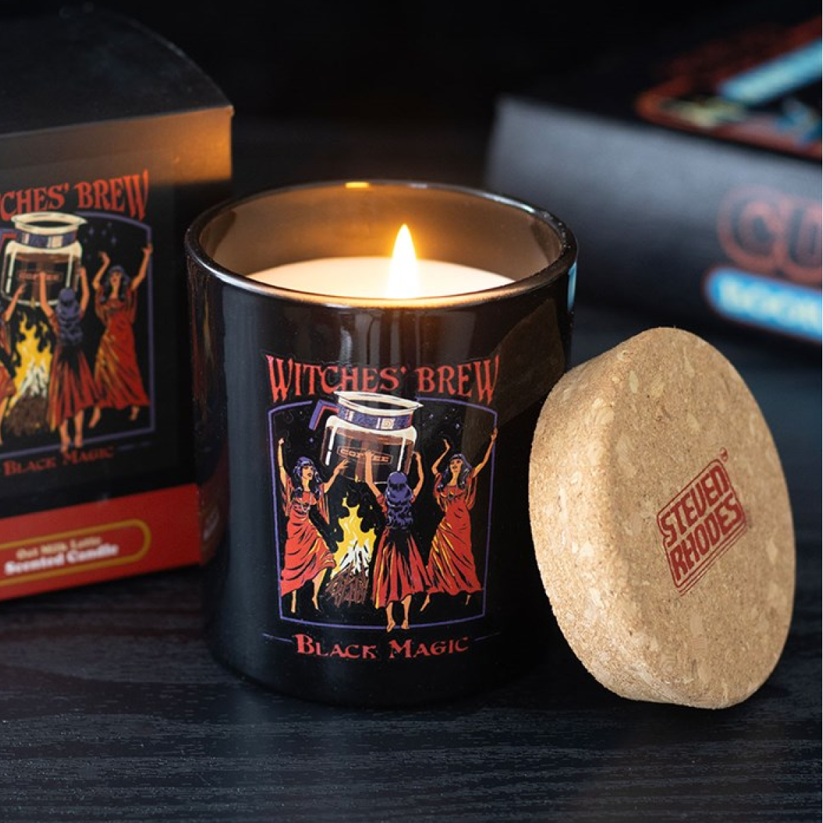 Candle labeled 'Witches' Brew Black Magic' with a cork lid and branded box in the background.